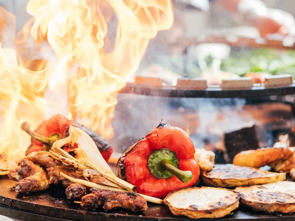 Grillakademie in der Marienburg in Monheim am Rhein Verschiedene Gemüsesorten braten auf einem großen Grill feurig, darunter rote Paprika und Zwiebeln.