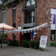 Cafe Im Dorf in Haan-Gruiten Ein Café mit roter Backsteinfassade, schattenspendendem Sonnenschirm und dekorativen Girlanden.