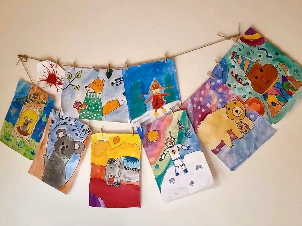Malzauber-Malkurse Kreative Kinderzeichnungen an einer Schnur aufgehängt, präsentieren bunte Tiere und fantasievolle Szenen.