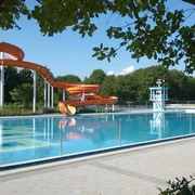 Stadtbad Langenfeld Orange Wasserrutsche im Freibad Langenfeld neben einem klaren Becken, umgeben von Bäumen und Gelände.