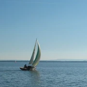 Wassersport Segelboot mit buntem Segel gleitet bei blauem Himmel über einen ruhigen, weitläufigen See.