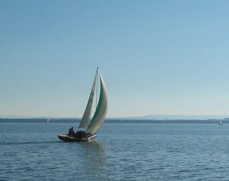 Wassersport Segelboot mit buntem Segel gleitet bei blauem Himmel über einen ruhigen, weitläufigen See.