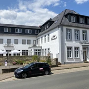 Hotel Riesenbeck Gebäude (2).jpg Weißes, zweistöckiges Gebäude mit Schieferdach und Hotel-Riesenbeck-Logo, davor ein geparktes Auto.