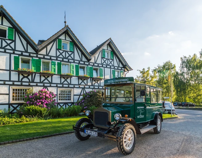 Lohmanns Romantik Hotel Gravenberg in Langenfeld Historisches Hotel mit grünen Fensterläden und Oldtimer im Vordergrund, umgeben von Landschaft.
