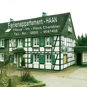 Ferienappartement Haaa Fachwerkhaus mit grünen Fensterläden und Werbeschrift in ländlicher Umgebung. Parkplatz davor.