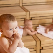 SWO_BabySauna_132.jpg Drei Babys entspannen auf Holzbänken in einer Sauna; eines kaut auf einem Handtuch, zwei ruhen dahinter.Three babies relax on wooden benches in a sauna; one chews on a towel, two rest behind it.Drie baby's relaxen op houten banken in een sauna; één kauwt op een handdoek, twee rusten erachter.