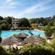 Waldbad in Hilden Freibad mit Schwimmbecken, Rutschen und Strohdächern, umgeben von dichten Bäumen im Waldbad Hilden.