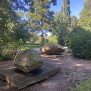 Große Findlinge auf Sandwegen in einem grünen Park, umgeben von Bäumen und Sträuchern.