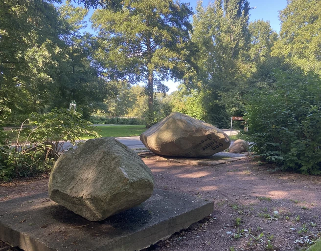 Findlingsgarten Große Findlinge auf Sandwegen in einem grünen Park, umgeben von Bäumen und Sträuchern.