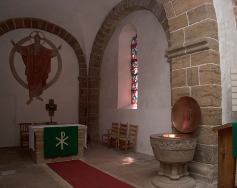 Im Inneren der Kirche Buchholz sind der Altar mit hohem Kreuz und ein farbenreiches Fenster zu sehen.