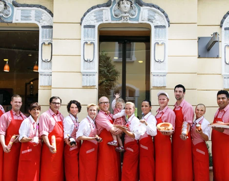 Metzgerei Rauschmann in Haan-Gruiten Eine Gruppe von Menschen in roten Schürzen steht lächelnd vor einem Gebäude mit verzierten Fenstern.