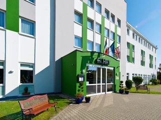 ACHAT Hotel in Monheim am Rhein Modernes Hotelgebäude mit grün-weißer Fassade, großer Eingangstür und mehreren Landesflaggen.