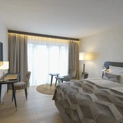 Essensio Hotel in Erkrath Ein modernes Hotelzimmer mit Doppelbett, Schreibtisch, Fernseher, Vorhängen und gemütlichen Sitzgelegenheiten.
