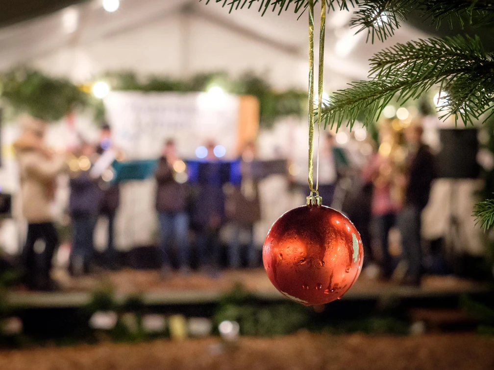 Rote Weihnachtskugel im Vordergrund, im Hintergrund unscharfe Live-Musikgruppe bei abendlicher Festbeleuchtung.