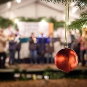 Adventsplaetzchen.jpg Rote Weihnachtskugel im Vordergrund, im Hintergrund unscharfe Live-Musikgruppe bei abendlicher Festbeleuchtung.
