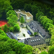 Waldhotel Heiligenhaus Luftaufnahme eines von Wald umgebenen Hotels mit Tennisplatz und moderner Gebäudeerweiterung.