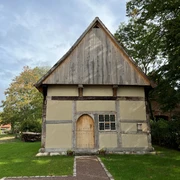 Pastorenhaus Martfeld Ein altes Fachwerkgebäude mit Satteldach und Holztür, umgeben von Bäumen und einem gepflasterten Weg.