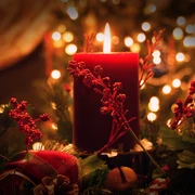 Rote Kerze im Vordergrund auf festlichem Adventskranz, umgeben von roten Beeren und weihnachtlichem Glanz.
