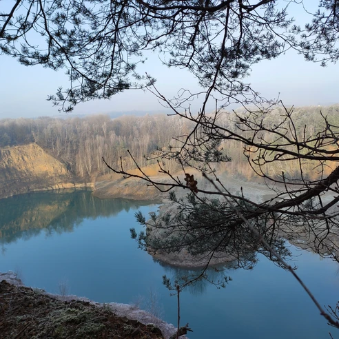 Steinbruch mit See Geopark mit See und Bäumen, ruhige Wasseroberfläche und bewaldete Ufer im Hintergrund.