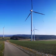 Windräder auf der Hüwe Windräder auf grünen Hügeln unter klarem Himmel, mit einem asphaltierten Weg im Vordergrund.