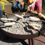 Stockbrot auf dem Abenteuerspielplatz Monheim Stockbrot backt über glühender Kohle in einer Feuerschale, umgeben von Kindern mit langen Stöcken.