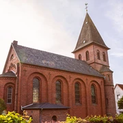 St.Johannis Kirche  Backsteinkirche St. Johannis mit spitzem Turmdach und Rundbogenfenstern, umgeben von grünen Büschen.