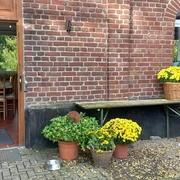 Bauernhof-Café Groß Ilbeck in Ratingen Eingang eines roten Backsteingebäudes mit offenen Holztüren, blühenden gelben Chrysanthemen in Körben.