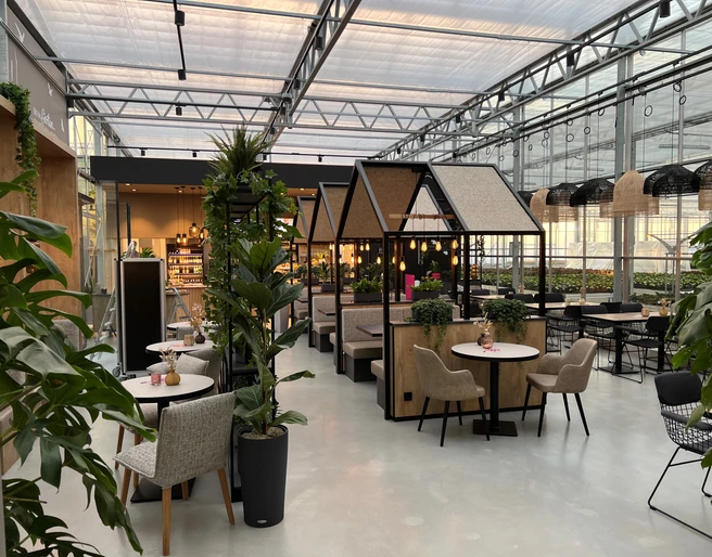 Café Karl Nienburg Geräumiges Café mit moderner Einrichtung, grünen Pflanzen und gemütlichen Sitznischen in Gewächshaus-Optik.