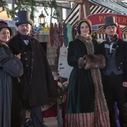 Viktorianischer Weihnachtsmarkt am Biedermeierstrand - Weihnachten in der Region Leipzig Vier Personen in viktorianischer Kleidung vor einem festlich geschmückten Verkaufsstand.