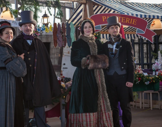 Viktorianischer Weihnachtsmarkt am Biedermeierstrand - Weihnachten in der Region Leipzig Vier Personen in viktorianischer Kleidung vor einem festlich geschmückten Verkaufsstand.