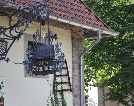 Altes Brauhaus zu Fallersleben Altes Fachwerkhaus mit verziertem schmiedeeisernem Schild in ruhiger, grüner Umgebung.