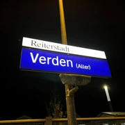 Bahnhof Verden Ein nachts beleuchtetes Bahnhofsschild mit der Aufschrift "Reiterstadt Verden (Aller)".