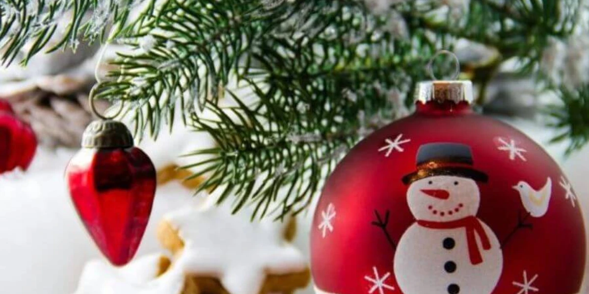 Weihnachtskugel.jpg Rot-weiße Weihnachtskugel mit Schneemann, hängend an Tanne, daneben rote Herzornamente und Kekse.