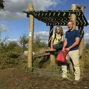 Steinhagen-Hörstation-Teutoburger-Wald-Tourismus-F-Grawe (3)_klein.jpg Ein Paar steht mit Wanderausrüstung bei einer hölzernen Raststation im Teutoburger Wald.