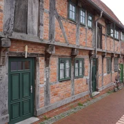 Budenhäuser Verden Fachwerkhäuserzeile aus rotem Backstein in Verden, mit grünen Türen und Fenstern an einer gepflasterten Straße.