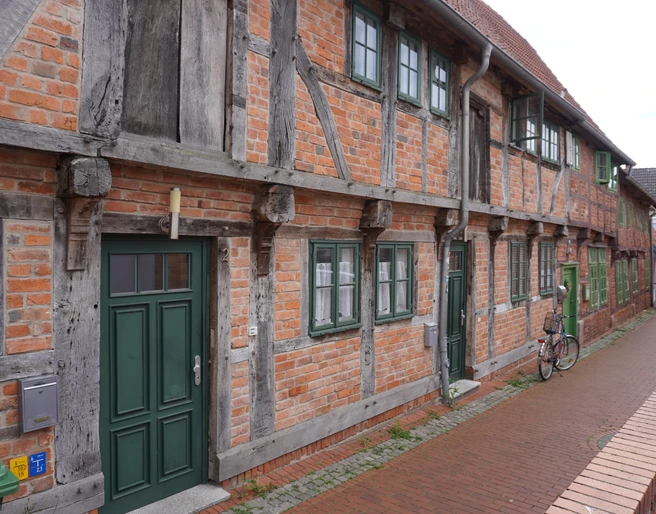 Budenhäuser Verden Fachwerkhäuserzeile aus rotem Backstein in Verden, mit grünen Türen und Fenstern an einer gepflasterten Straße.