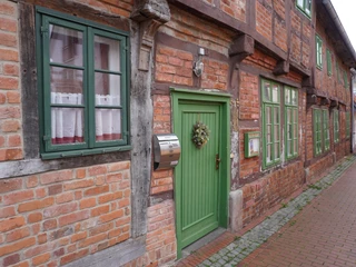 Budenhäuser Verden Fachwerkhäuser mit roten Ziegelwänden, weißen Fenstern und grünen Türen entlang einer Pflastergasse.