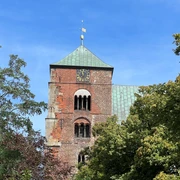 Dom Verden Roter Backstein-Dom mit grünem Dach, Uhr und Türmen umrahmt von dichten grünen Bäumen.