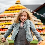 Herbst auf dem Krewelshof Ein lächelndes Mädchen posiert vor einer großen, bunten Pyramide aus Kürbissen verschiedener Farben.