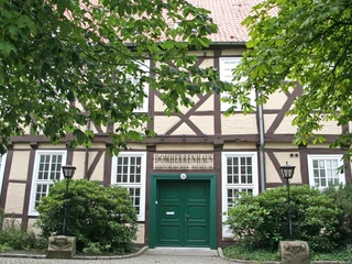 Museum Domherrenhaus Fachwerkhaus mit grünem Eingang, großen Fenstern, umgeben von Bäumen und Laternen; Museumsschild.