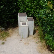 John Lennon-Denkmal Verden Grau-verwitterte Skulptur zu Ehren von John Lennon, eingebettet in grünen Büschen an einem sandigen Weg.