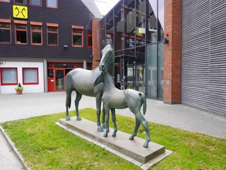 Skulptur Mutterstute mit Fohlen Verden Die Skulptur einer Mutterstute mit Fohlen steht vor einem modernen Gebäude in Verden.
