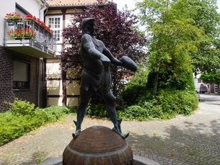 Störtebeker-Brunnen Bronzestatue eines Piraten mit Schwert, umgeben von Hecken und Gebäuden in einer gepflasterten Passagen.