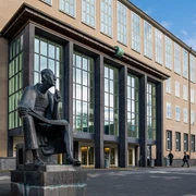 Albertus Magnus Monument Das Albertus-Magnus-Denkmal, eine bronzene Statue des sitzenden Gelehrten, vor einer modernen Gebäudeansicht in Köln.The Albertus Magnus monument, a bronze statue of the seated scholar, in front of a modern building in Cologne.