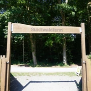 Stadtwaldfarm Verden Eingang zur Stadtwaldfarm Verden mit hölzernem Torbogen, umgeben von grünen Bäumen im Hintergrund.