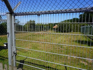 Storchenpflegestation Verden Ein weitläufiges, begrüntes Gehege mit Drahtzaun und blauem Himmel, geeignet für Vogelpflege.