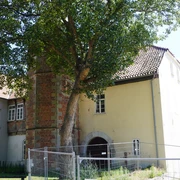 Syndikatshof Ein großes Gebäude mit Backsteinmauer und Torbogen, flankiert von einem hohen Baum und Zaun.
