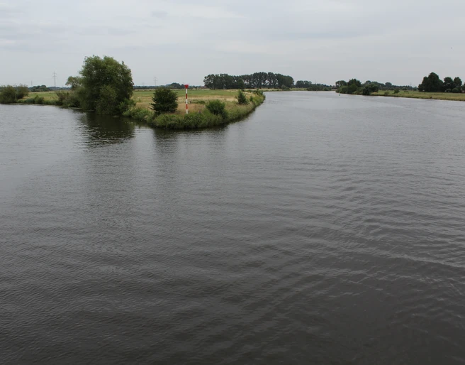 Allermündung Mündung der Aller in die Weser mit ruhigem Wasser, grünen Ufern und leicht bewölktem Himmel.