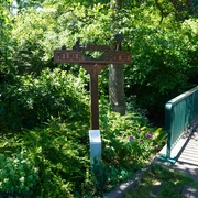 Eitzer Wegweiser Ein hölzerner Wegweiser neben einer grünen Brücke, umgeben von dichtem, üppigem Laub.