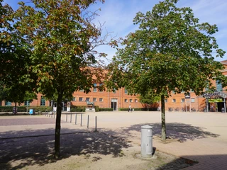Roter Backsteinbau am Holzmarkt Verden mit grünen Bäumen im Vordergrund unter blauem Himmel.